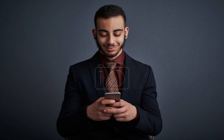 Photo for Communication is the key to any successful business. Studio shot of a stylish young businessman sending a text message while standing against a gray background - Royalty Free Image