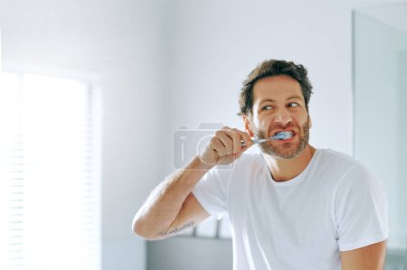 Téléchargez les photos : Je me prépare pour la journée à venir. un bel homme d'âge moyen se brossant les dents dans la salle de bain à la maison - en image libre de droit