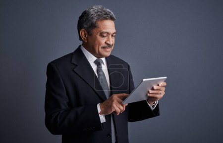 Photo for Staying in synch with my office computer. Studio shot of a mature businessman using his digital tablet - Royalty Free Image