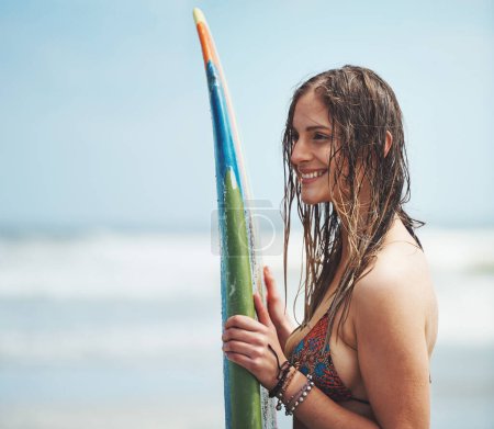 Téléchargez les photos : Elle vit pour surfer. une jolie jeune femme debout sur une plage avec une planche de surf - en image libre de droit