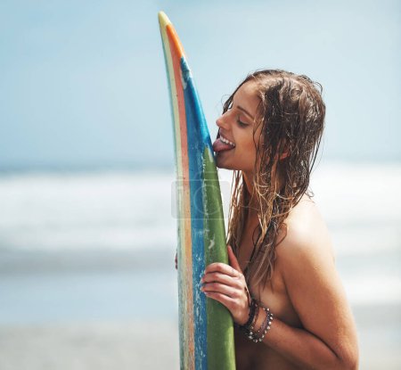 Foto de Que necesita un novio cuando tienes una tabla. una atractiva joven de pie en una playa lamiendo su tabla de surf - Imagen libre de derechos