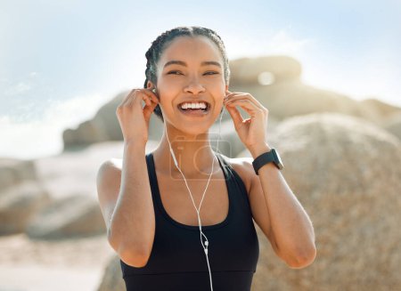 Foto de Mujer feliz con auriculares, fitness en la playa y escuchar música para la motivación y el entrenamiento al aire libre. Ejercicio, salud y sonrisa, atleta femenina en streaming en línea con radio y audio en la naturaleza. - Imagen libre de derechos