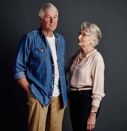Téléchargez les photos : Il sait ce qu'il a fait... Portrait en studio d'un couple de personnes âgées affectueux posant sur un fond gris - en image libre de droit