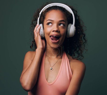 Photo for Music, headphones and gen z girl in studio for streaming, silly face or audio on green background. Podcast and goofy female model relax while listening to radio, audio or online playlist. - Royalty Free Image