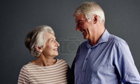 Foto de Prometí no dejarte nunca... toma de estudio de una pareja mayor cariñosa posando sobre un fondo gris - Imagen libre de derechos