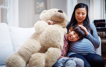 Photo for I cant wait to meet my brother or sister. Cropped portrait of a little girl sitting with her mother and her teddybear on the sofa - Royalty Free Image
