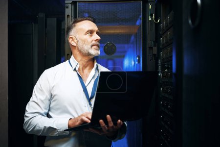 Photo for Working on the main connection. a mature man using a laptop while working in a server room - Royalty Free Image