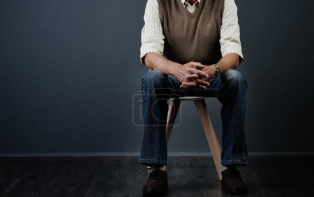 Photo for Waiting patiently. Studio shot of an unrecognizable man sitting on a wooden stool against a dark background - Royalty Free Image