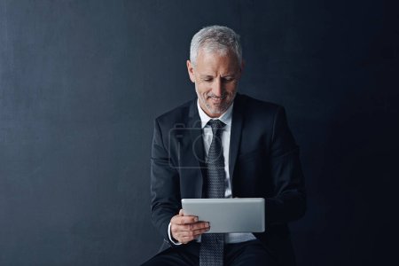 Photo for His entire business is the palm of his hand. Studio shot of a mature businessman using a digital tablet against a dark background - Royalty Free Image