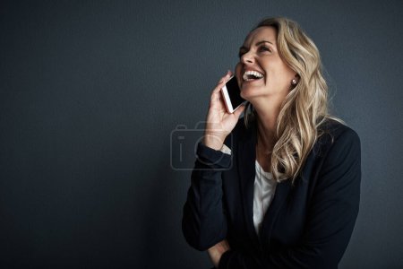 Foto de Suena como si hubiera tenido otro éxito. Captura de estudio de una mujer de negocios madura hablando en un teléfono celular sobre un fondo gris - Imagen libre de derechos