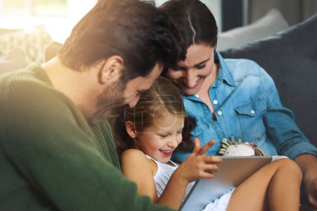 Téléchargez les photos : Profiter du wifi ensemble. une jeune famille utilisant une tablette et se refroidissant sur le canapé ensemble à la maison - en image libre de droit