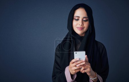 Téléchargez les photos : Garder son style de vie mobile. Plan studio d'une jeune femme portant une burqa et utilisant un téléphone portable sur fond gris - en image libre de droit