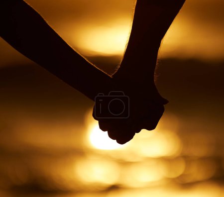 Téléchargez les photos : Couple, silhouette et se tenant la main au coucher du soleil sur une plage pour des vacances ou des vacances en plein air. Gros plan de l'homme et de la femme dans la nature pour la paix, le calme et l'amour de l'océan pour l'ombre créatrice, le voyage ou la liberté. - en image libre de droit