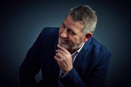 Photo for Now theres an idea...Studio shot of a confident and mature businessman sitting with his hand on his chin against a dark background - Royalty Free Image