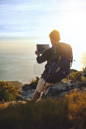 Téléchargez les photos : C'est une aire de jeux pour adultes. un jeune homme utilisant une tablette numérique lors d'une randonnée en montagne - en image libre de droit