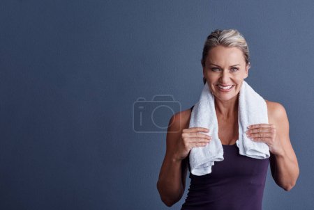 Foto de Sólo necesito mi tiempo. Retrato de estudio de una atractiva mujer madura en ropa deportiva de pie con una toalla alrededor de su cuello sobre un fondo azul - Imagen libre de derechos