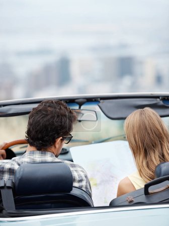 Photo for I think we should go this way next...Rear view of a young couple in their convertible checking a map - Royalty Free Image