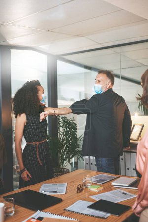 Photo for Safety is our primary focus. two businesspeople standing together and elbowing each other while wearing face masks during a meeting in the office - Royalty Free Image