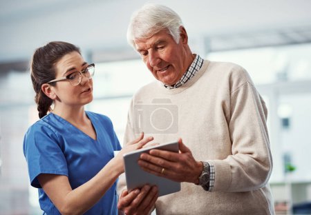 Téléchargez les photos : Donc je peux garder une trace de toutes mes informations ici. une jeune infirmière et sa patiente âgée regardant une tablette à la maison de retraite - en image libre de droit