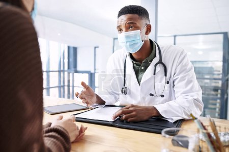 Photo for Did you eat or drink anything this morning. a young doctor sitting with his patient and wearing his face mask during a consultation in the clinic - Royalty Free Image