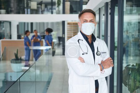 Photo for Lets get you healthy again. Cropped portrait of a handsome mature doctor wearing a face mask and standing alone in the clinic - Royalty Free Image