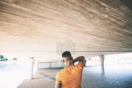 Photo for Nothing compromises progress like pain. Rearview shot of a young man experiencing neck pain while working out against an urban background - Royalty Free Image