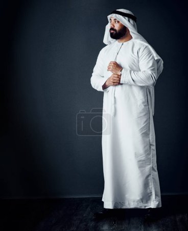 Téléchargez les photos : Ses aspirations le guident. Plan studio d'un jeune homme vêtu de vêtements traditionnels islamiques posant sur un fond sombre - en image libre de droit