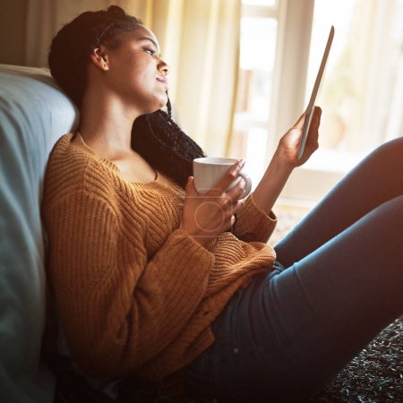 Téléchargez les photos : La façon moderne d'échapper aux pressions de l'époque. une jeune femme détendue buvant du café et utilisant une tablette numérique à la maison - en image libre de droit