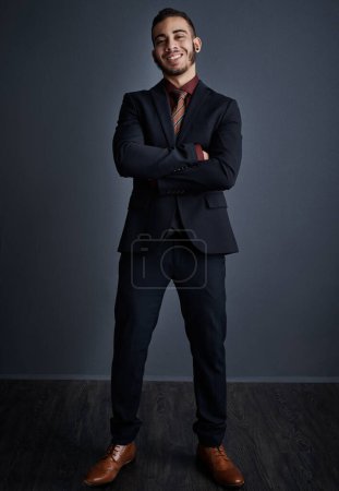 Foto de El jefe ha vuelto. Retrato de estudio de un joven y elegante hombre de negocios de pie con los brazos cruzados sobre un fondo gris - Imagen libre de derechos