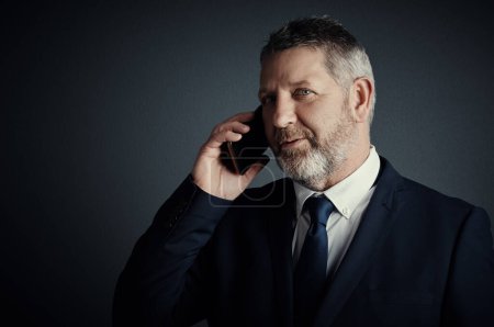 Photo for Ill call you back...Studio shot of a handsome mature businessman looking thoughtful while making a call against a dark background - Royalty Free Image