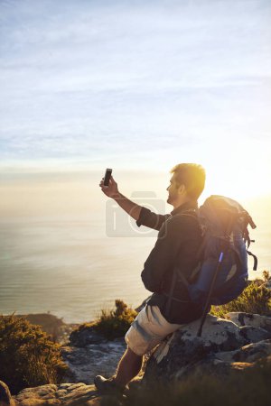 Téléchargez les photos : Le soleil se couche, les selfies sortent. un jeune homme faisant des selfies en montant une montagne - en image libre de droit