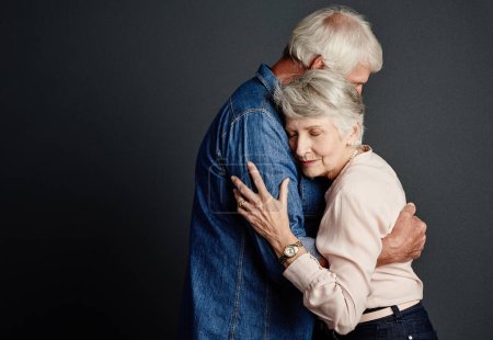 Foto de A salvo en sus brazos. Estudio de una pareja de ancianos cariñosos posando sobre un fondo gris - Imagen libre de derechos