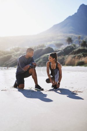 Photo for Starting their day out in the fresh air with some fitness. a sporty young couple tying their shoelaces while out for a run along the beach - Royalty Free Image