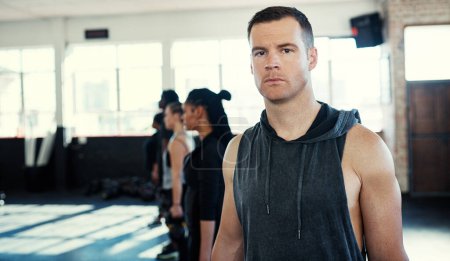 Photo for This is where I work. a focused group of young people standing in a row and training with weights while one looks into the camera in a gym - Royalty Free Image