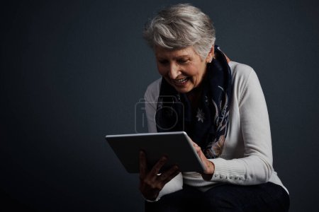 Téléchargez les photos : Je peux m'habituer à ça. Plan studio d'une femme âgée joyeuse debout et utilisant une tablette - en image libre de droit