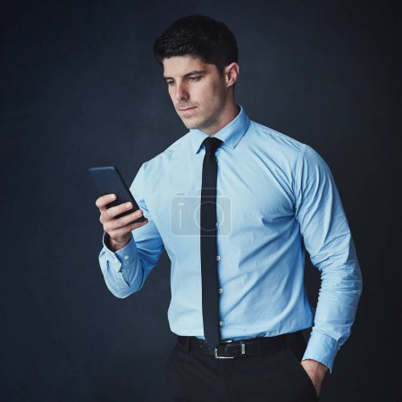 Photo for Every executive needs to be within reach. Studio shot of a young businessman texting on a cellphone against a dark background - Royalty Free Image