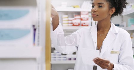 Foto de Esto es lo que necesitamos aquí. un joven farmacéutico atractivo sacando medicamentos recetados de un estante en un químico - Imagen libre de derechos