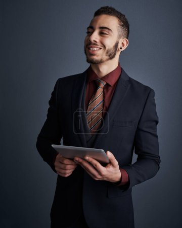 Foto de Aprovechando al máximo la tecnología. Estudio de un joven hombre de negocios con estilo que se ve reflexivo mientras se utiliza una tableta contra un fondo gris - Imagen libre de derechos