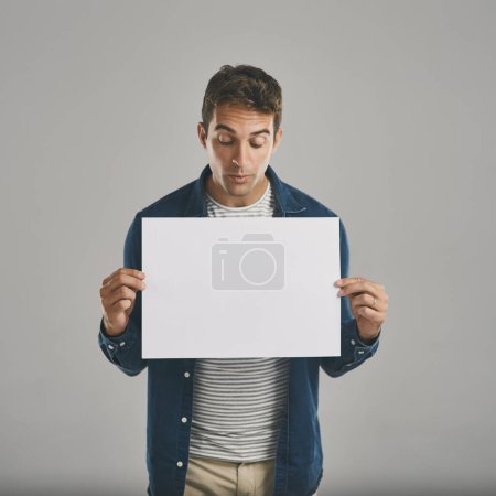 Photo for Ooh, what do we have here...Studio shot of a young man holding a blank placard against a grey background - Royalty Free Image