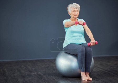 Foto de Manteniendo su fuerza. Tiro de longitud completa de una mujer mayor haciendo ejercicio con pesas mientras está sentada en una pelota de ejercicio - Imagen libre de derechos
