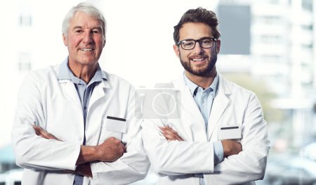 Foto de Dos generaciones de médicos. Retrato de dos alegres científicos varones de pie con los brazos cruzados mientras miran a la cámara dentro de un laboratorio - Imagen libre de derechos