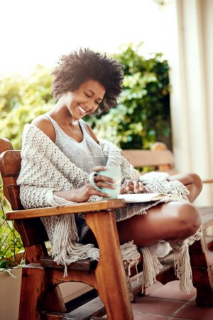 Foto de Mujer negra, lectura y patio trasero con libro y café sensación de relax y felicidad. La felicidad, la persona africana femenina y la sonrisa en el jardín de casa por la mañana con el té al aire libre al sol con la historia. - Imagen libre de derechos