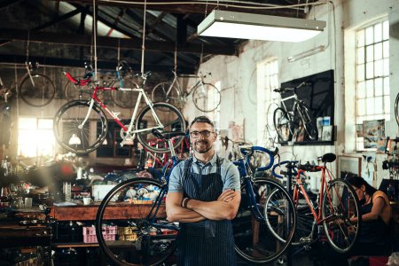 Foto de Hombre feliz, retrato y reparación en tienda de bicicletas con los brazos cruzados en el taller de la pequeña empresa. Propietario, mecánico de bicicletas y sonrisa de persona segura, técnico profesional o maduro y gafas en la tienda. - Imagen libre de derechos