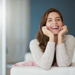 Portrait, happy and woman relax on sofa in home living room laughing at comedy. Face, smile or excited female person from Canada on couch in lounge, apartment or house to enjoy me time, joke or funny.
