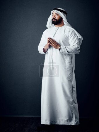 Foto de La determinación y la oración te llevarán allí. Estudio de un joven vestido con ropa tradicional islámica posando sobre un fondo oscuro - Imagen libre de derechos