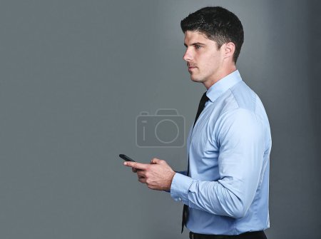Foto de Mantenerse en el buen camino con éxito. Captura de estudio de un joven hombre de negocios enviando mensajes de texto en un teléfono celular sobre un fondo gris - Imagen libre de derechos