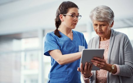 Téléchargez les photos : Voici vos antécédents médicaux. une jeune infirmière et sa patiente âgée regardant une tablette à la maison de retraite - en image libre de droit