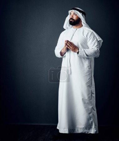 Photo for Pray for help then make it happen. Studio shot of a young man dressed in Islamic traditional clothing posing against a dark background - Royalty Free Image