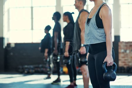 Photo for Follow my lead. a focused group of young people standing in a row and training with weights in a gym - Royalty Free Image