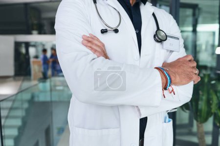 Téléchargez les photos : Déterminé à trouver un remède. un médecin méconnaissable debout les bras croisés dans la clinique pendant la journée - en image libre de droit